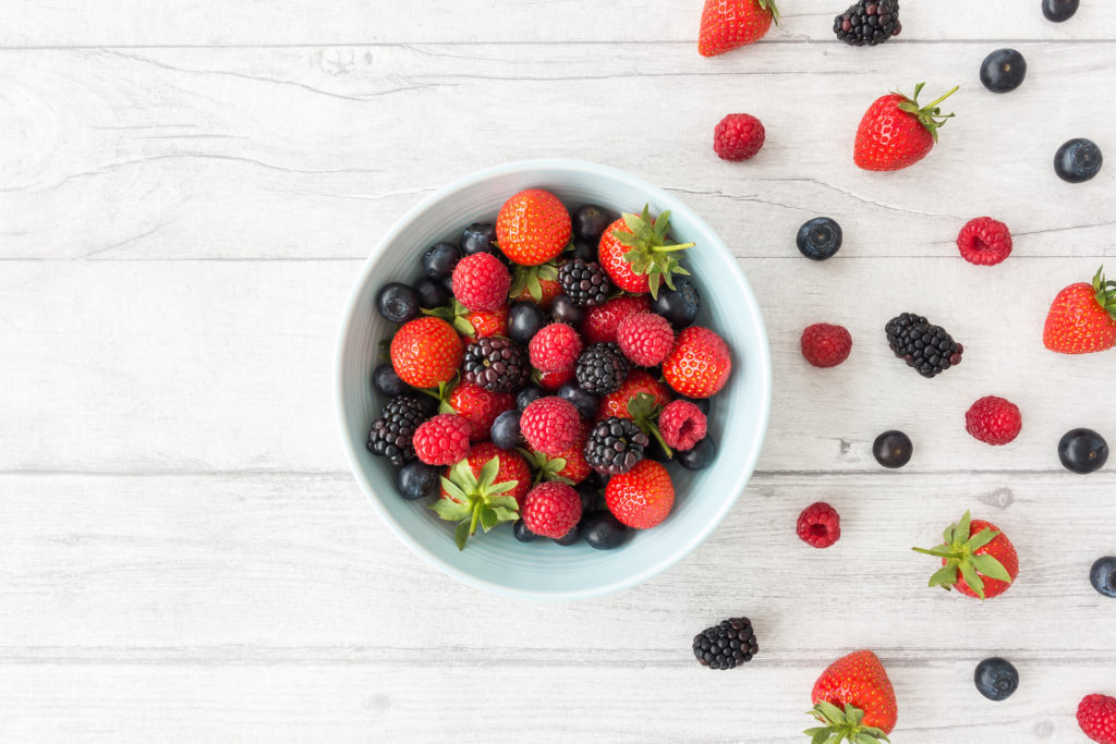 variety-of-fresh-summer-berries-in-a-blue-bowl-on-white-wood-bac
